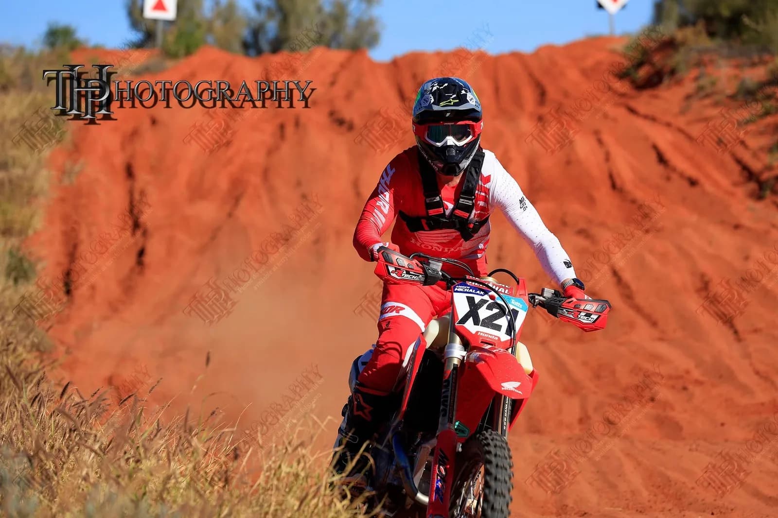 Andrew Michalak racing his Honda CRF at the Finke Desert Race in red riding gear, cresting a red sand mound.