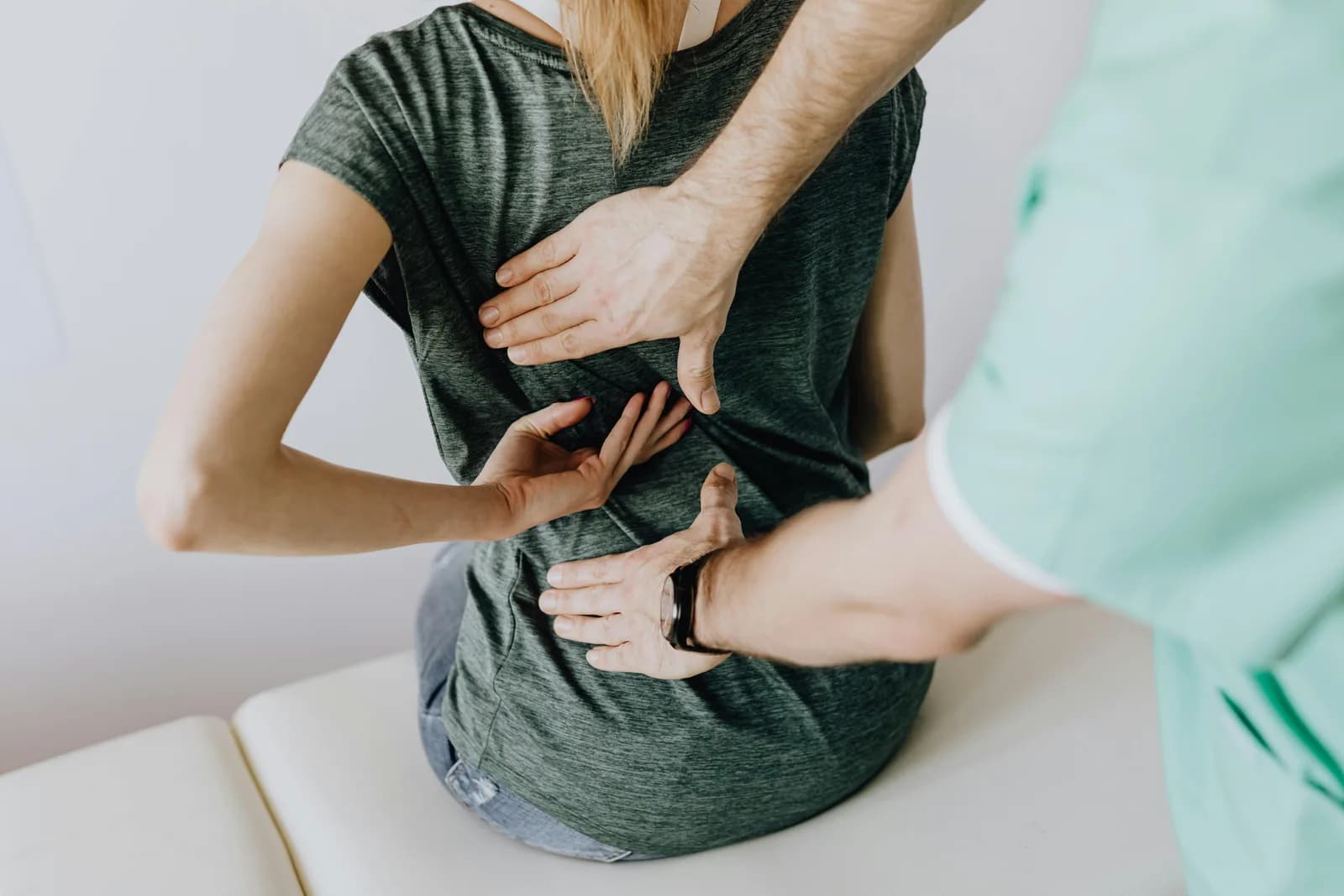A therapist assesses a client's lower back with both hands placed either side of the spine during a remedial massage consultation.