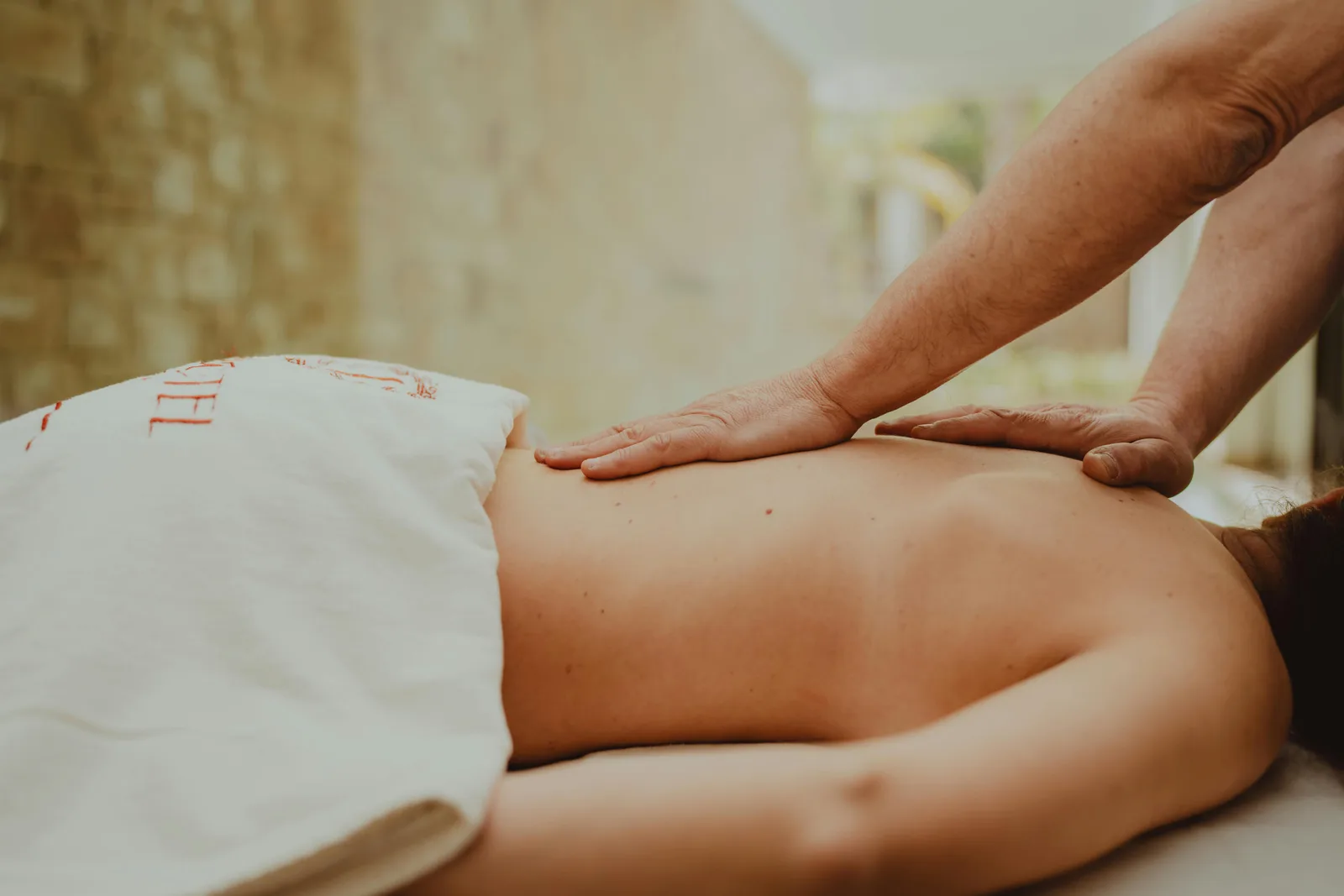 A client receiving a calm, two-handed back massage on the table in soft natural light.
