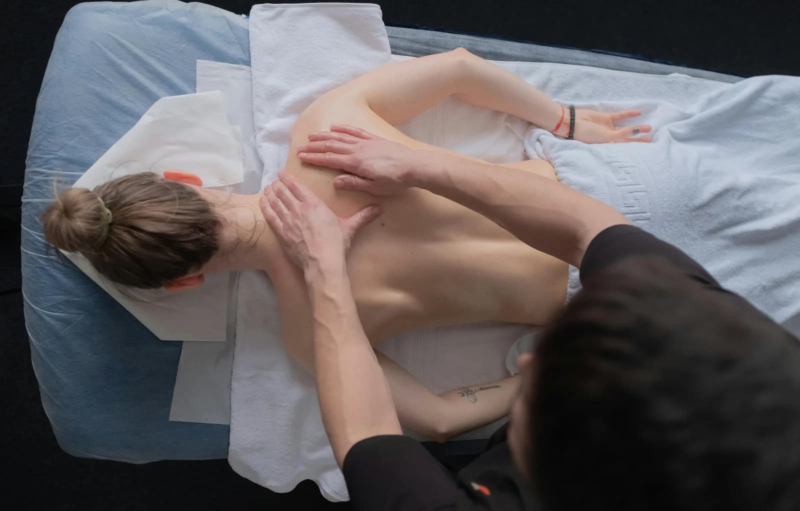 Overhead view of a remedial massage therapist working both hands across a client's upper back, shoulders and base of the neck.