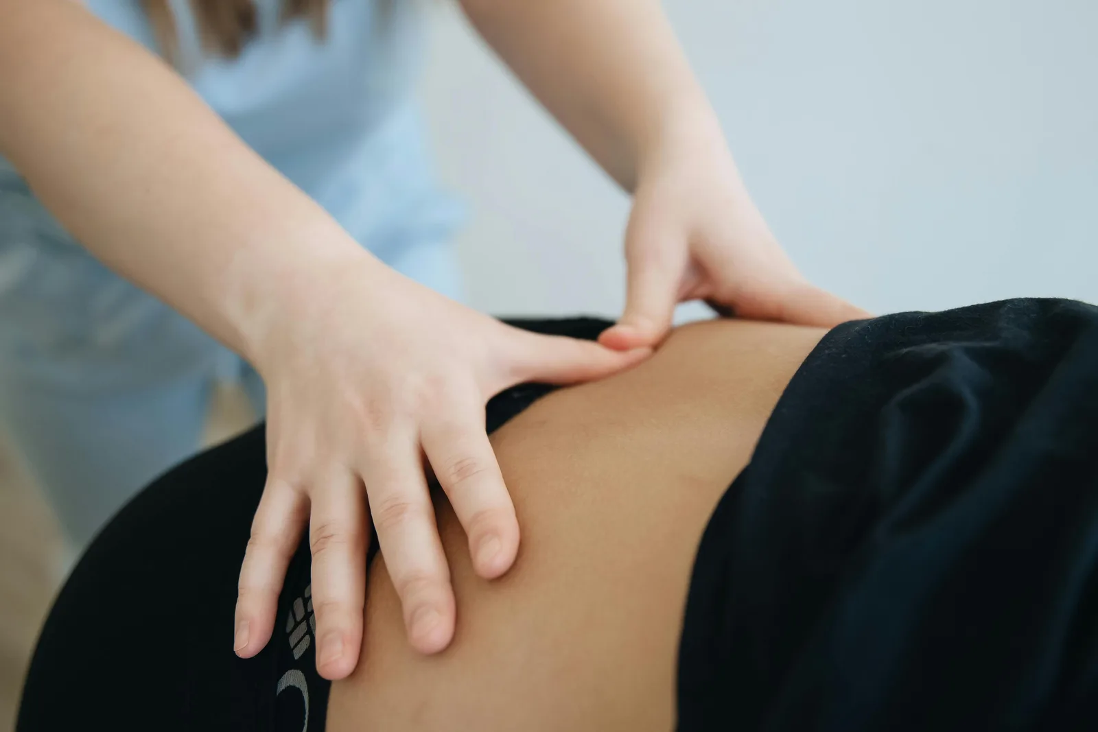 Close-up of a remedial massage therapist's hands working with sustained pressure across a client's lower back.