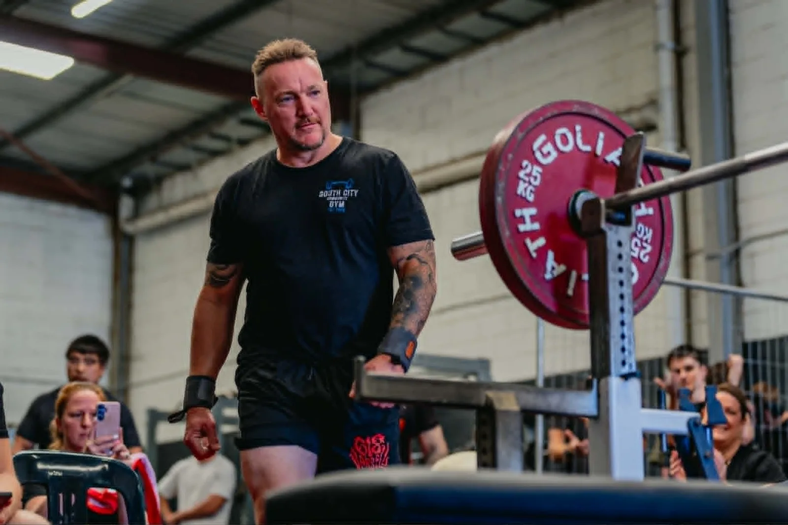 Nigel walking out from the bench press station at a sanctioned powerlifting competition, with spectators watching.