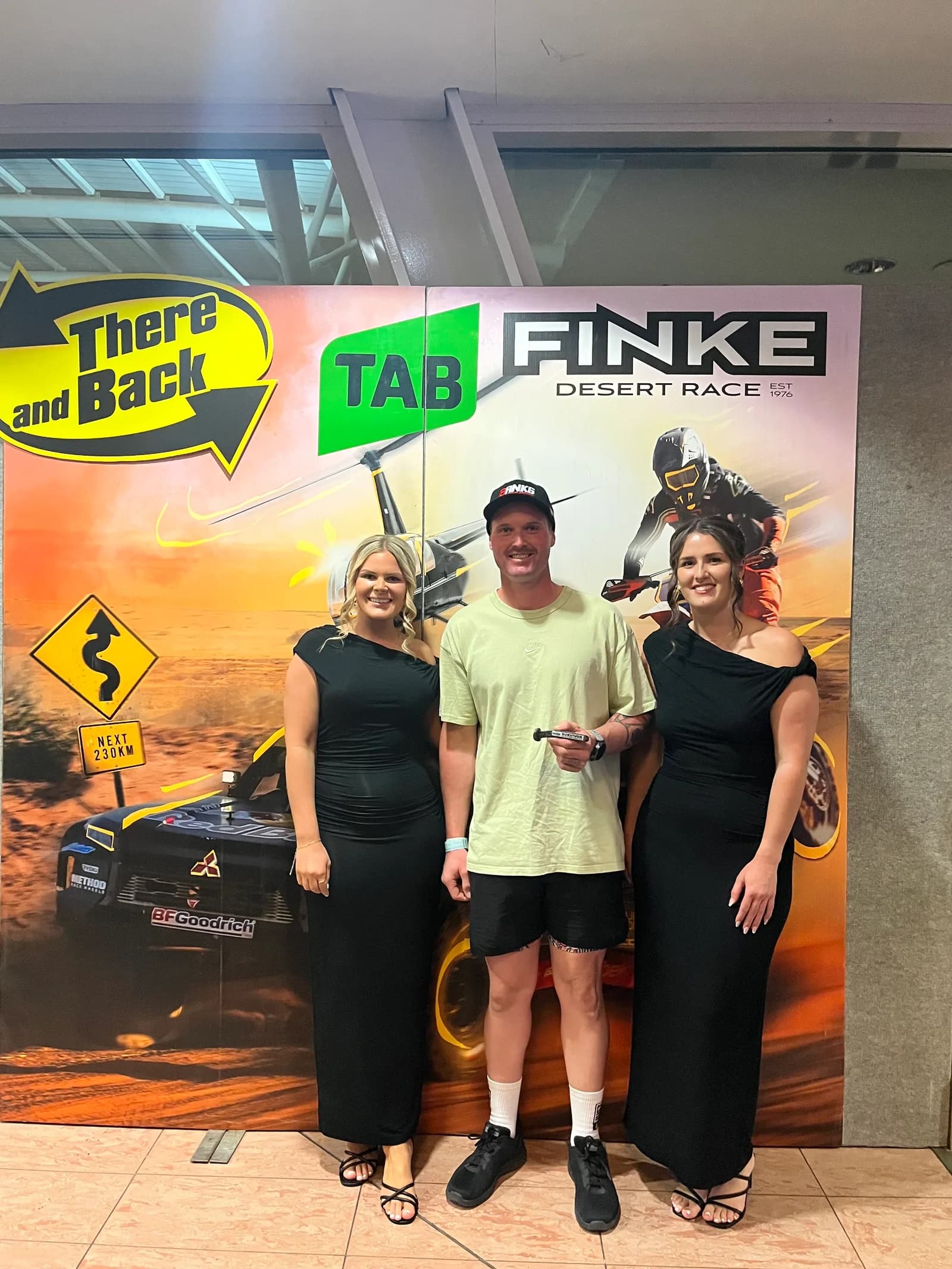 Andrew Michalak with Sarah Grapentin and a friend in front of the Finke Desert Race 'There and Back' banner at the event.